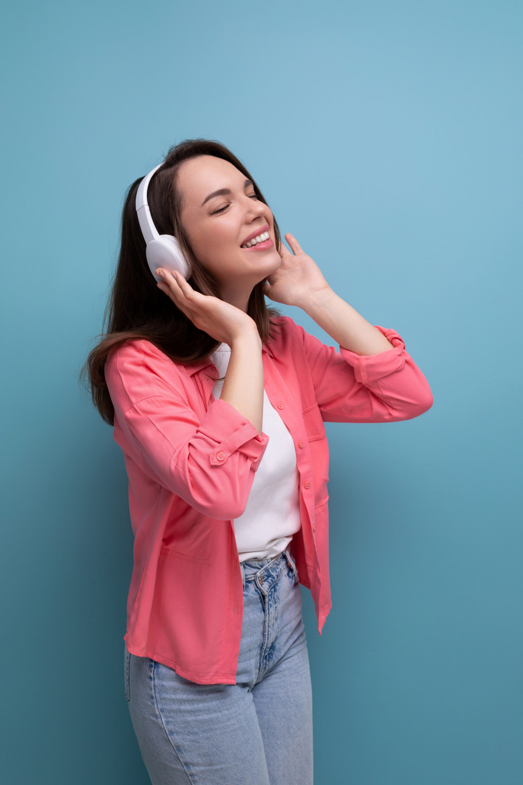 enjoying brunette young woman with dark hair below her shoulders in a shirt and jeans with wireless headphones.