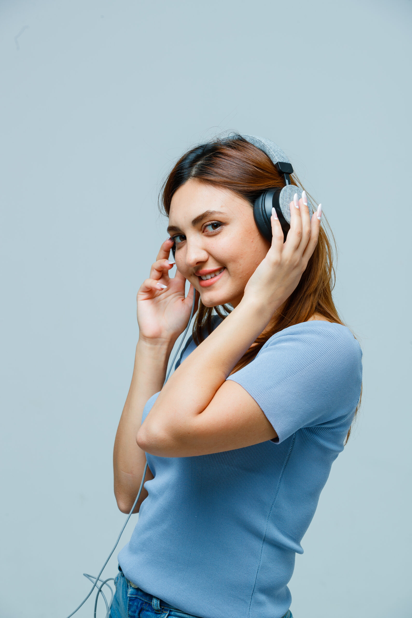young lady holding hands on headphones while listening to music in t-shirt and looking attractive. front view.