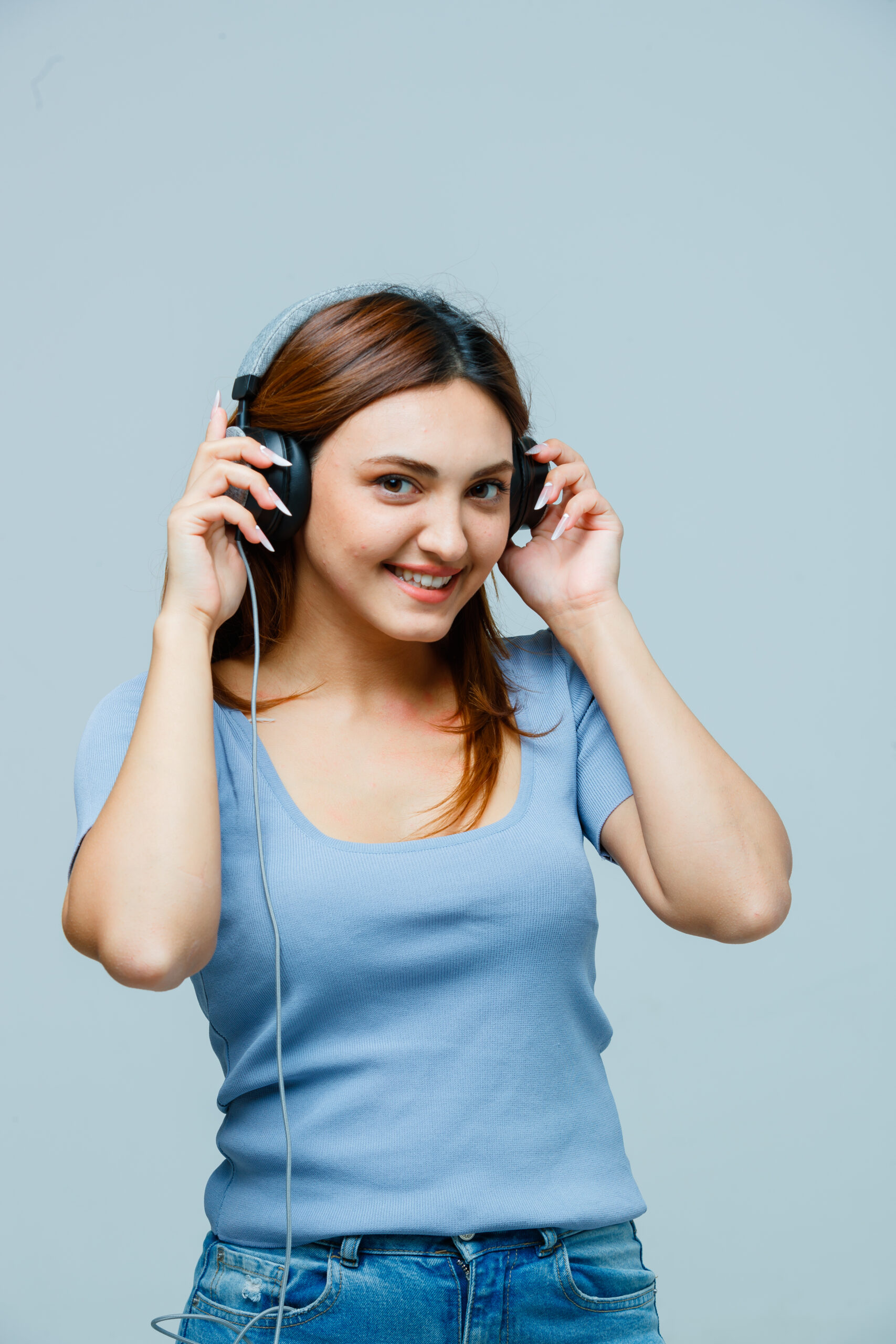 young lady holding hands on headphones while listening to music in t-shirt and looking happy. front view.