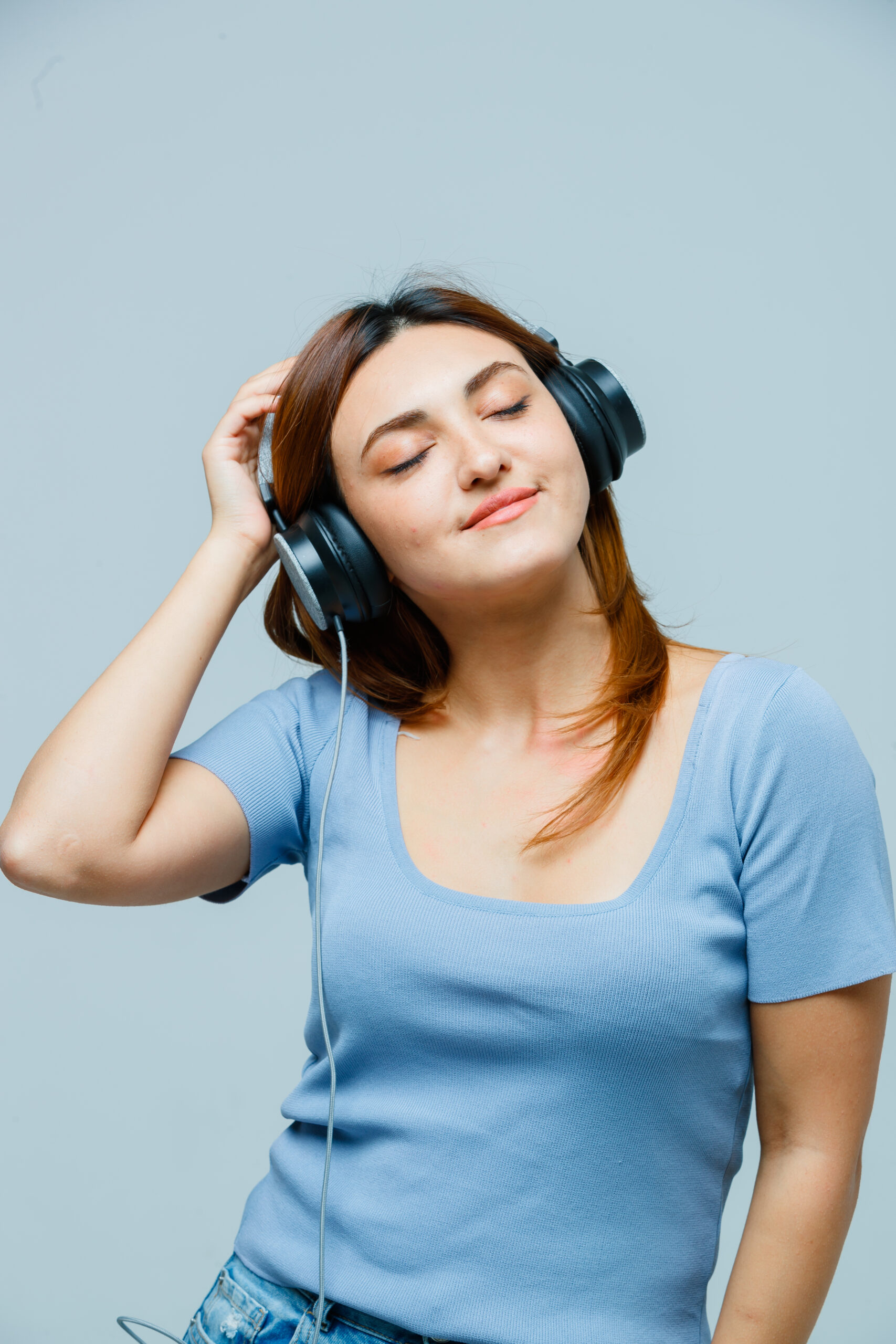 young lady listening to music with headphones in t-shirt and looking peaceful , front view.