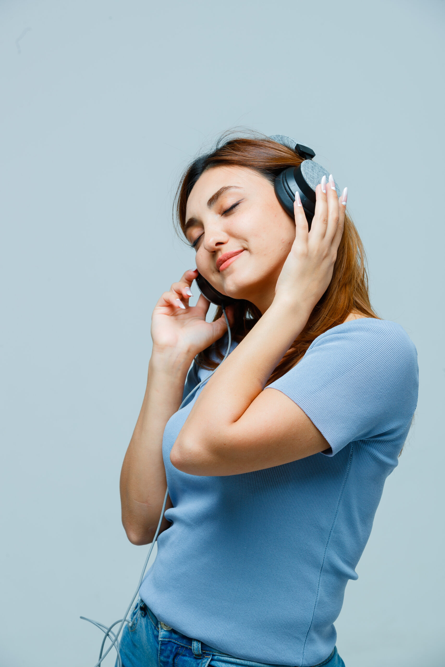 young lady listening to music with headphones in t-shirt and looking happy. front view.